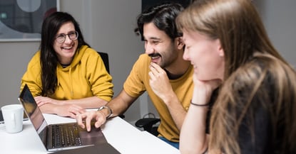 three people looking at a laptop and laughing