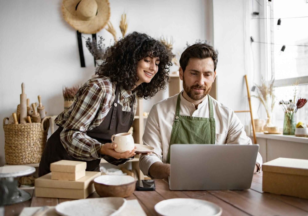 Woman and man wearing aprons looking at a laptop screen