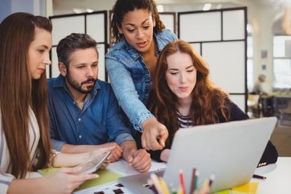 Businesswoman pointing at laptop with coworkers at desk in creative office-1