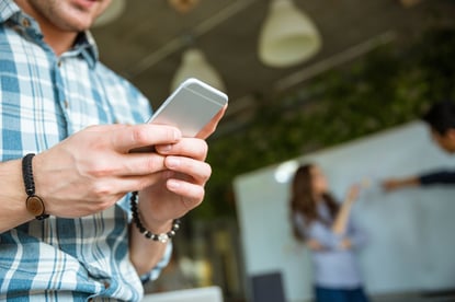 Closeup of hands of young man in checkered shirt using mobile phone while his partners arguing-2