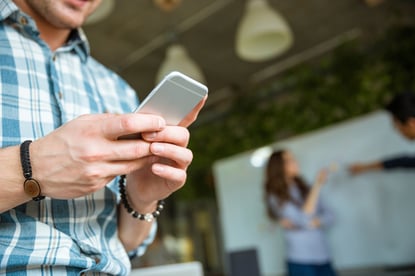 Closeup of hands of young man in checkered shirt using mobile phone while his partners arguing-4