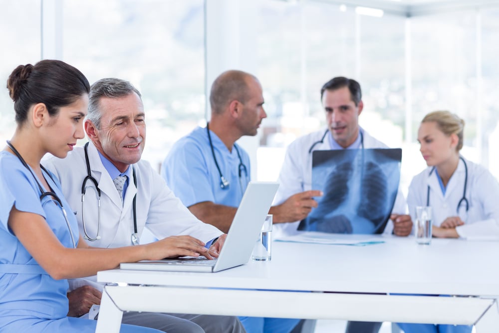 Doctors using computer whiles theirs colleagues looking at Xray in medical office-1