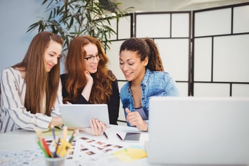 Smiling businesswomen looking at digital tablet at desk in creative office