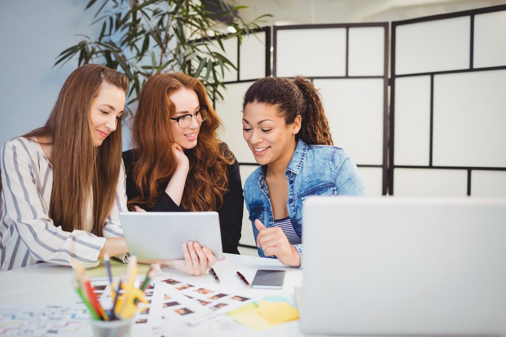 Smiling businesswomen looking at digital tablet at desk in creative office