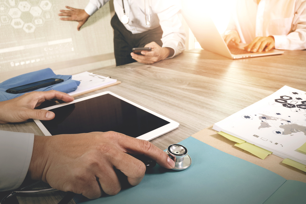 Medicine doctor hand working with modern computer and digital pro tablet with blank screen with his team on wooden desk as medical concept