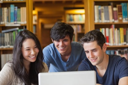 Students sitting looking at a laptop at the library