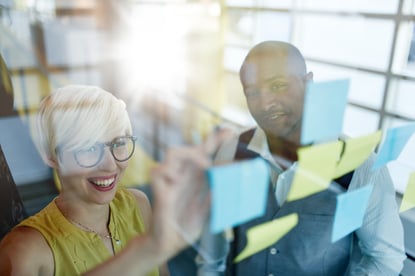 Two creative millenial small business owners working on social media strategy brainstorming using adhesive notes in windows-1