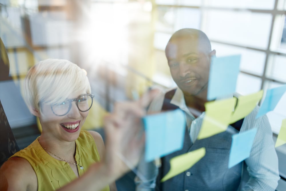 Two creative millenial small business owners working on social media strategy brainstorming using adhesive notes in windows-1