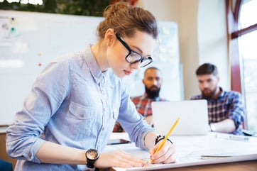 Woman engineer working on blueprint in office with colleagues on background-1