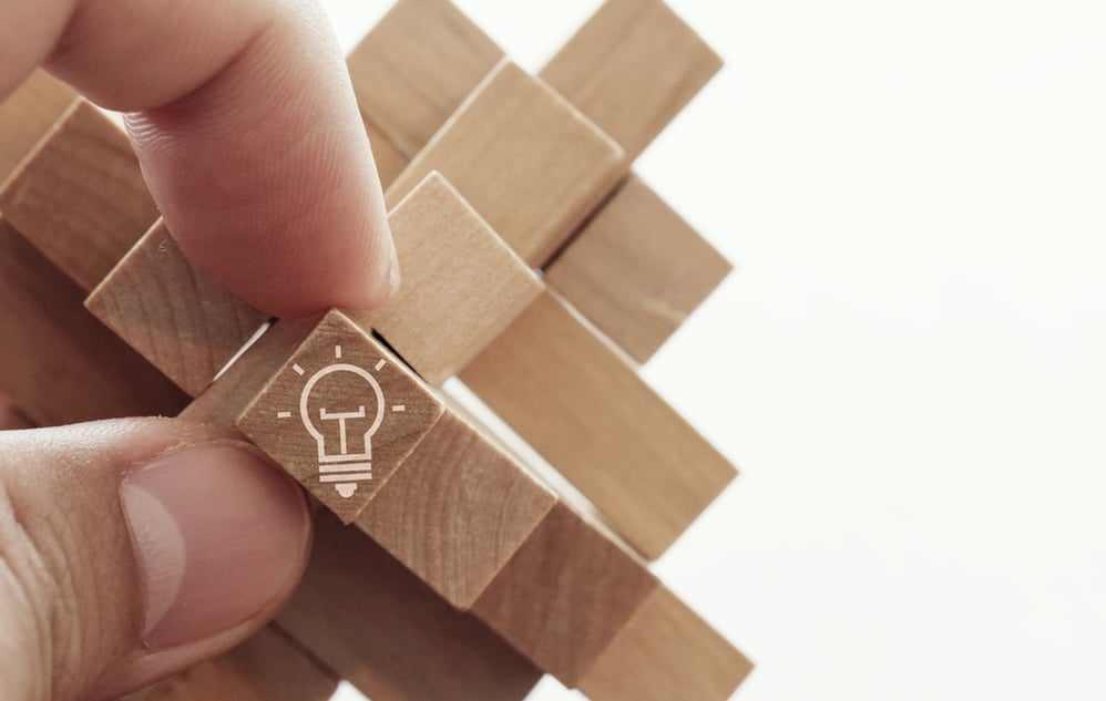 close up of hand showing illuminated light bulb icon on a wooden block puzzle as innovation concept